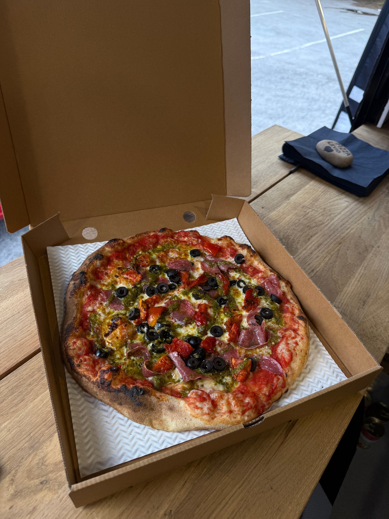 Pizza with cured meat, olives and pesto