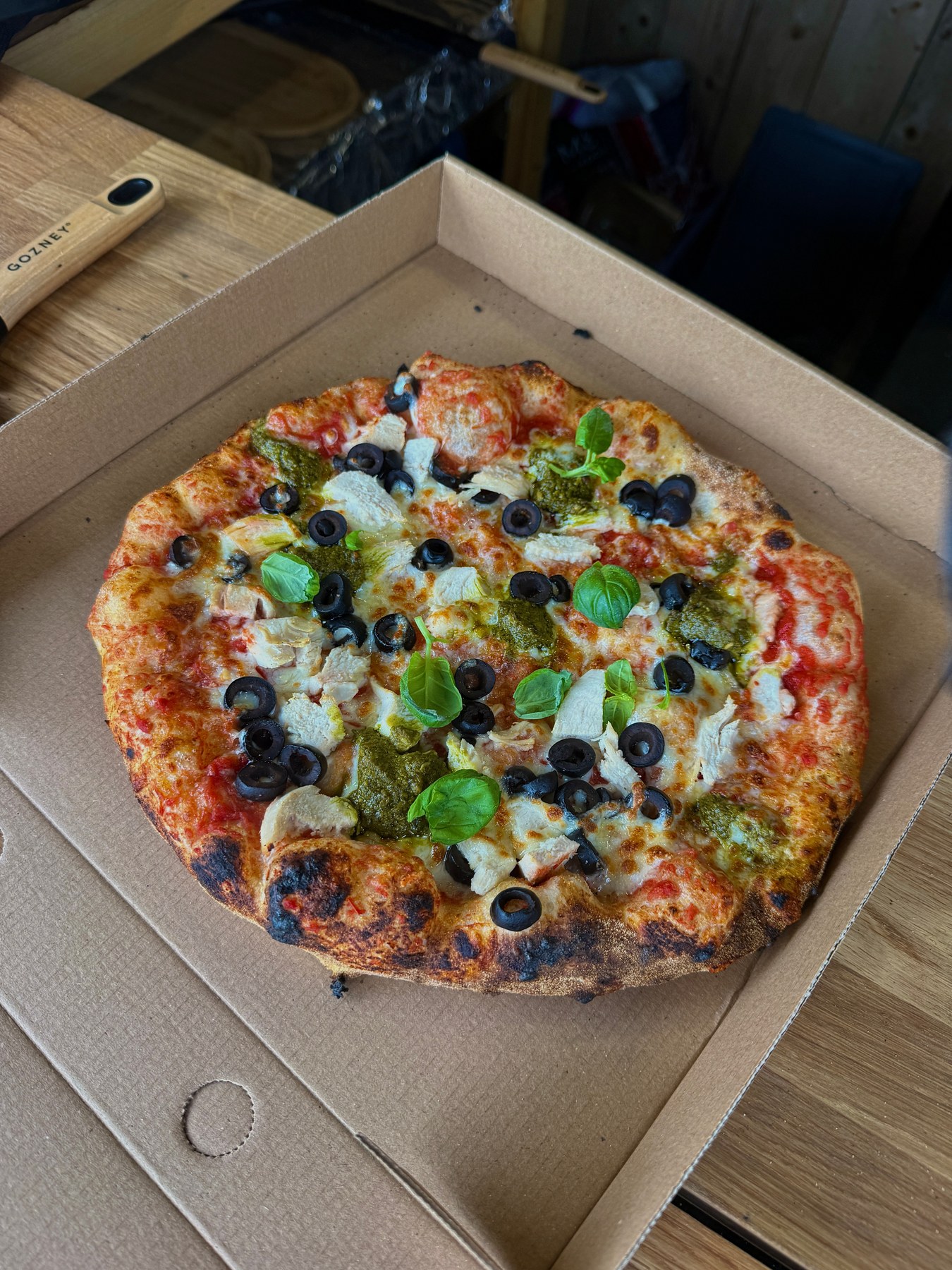 Pizza topped with chicken, olives, pesto and basil
